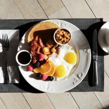 A delicious breakfast spread featuring eggs, bacon, fruit, and coffee on a sunlit table.