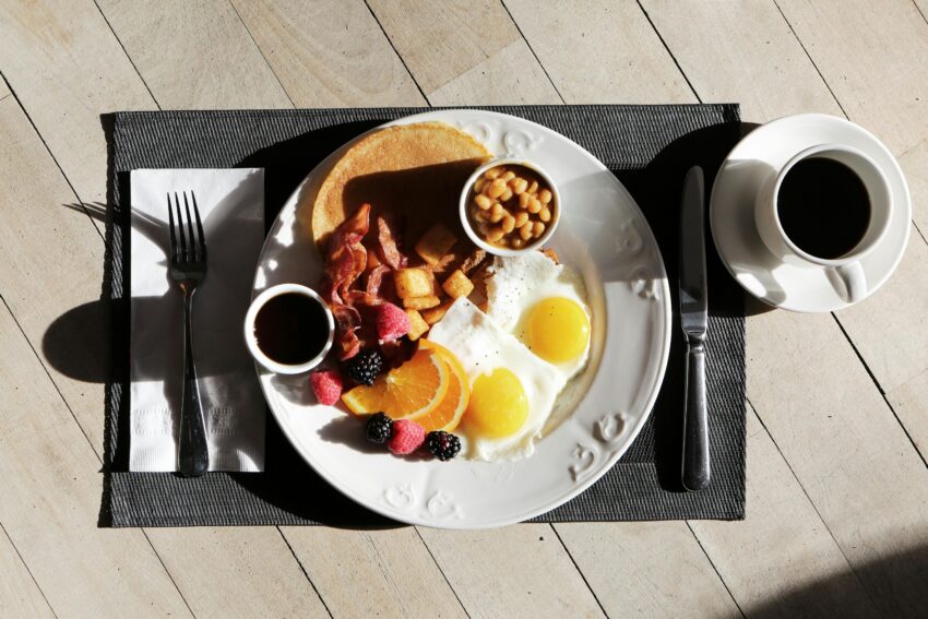 A delicious breakfast spread featuring eggs, bacon, fruit, and coffee on a sunlit table.