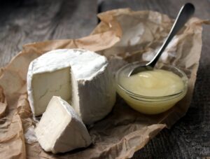 Close-up of gourmet soft cheese with a portion cut out, served with honey on rustic brown paper.