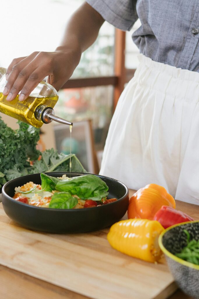 Person drizzles olive oil over fresh vegetable salad on a wooden cutting board.