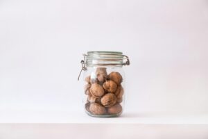 A clear glass jar filled with walnuts, isolated on a minimalist white background.