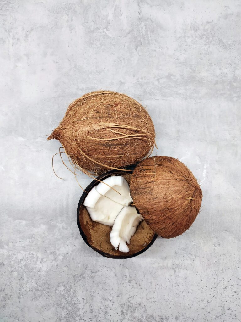 Fresh whole and sliced coconuts on a textured gray background, captured from above.