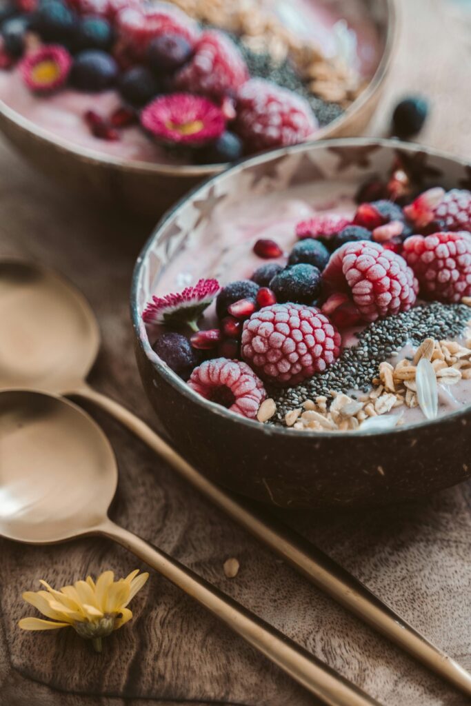 Delicious berry smoothie bowl topped with raspberries, blueberries, nuts, and seeds, accompanied by golden spoons.