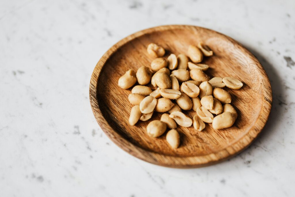 Top view of roasted peanuts in a wooden plate placed on a marble surface.