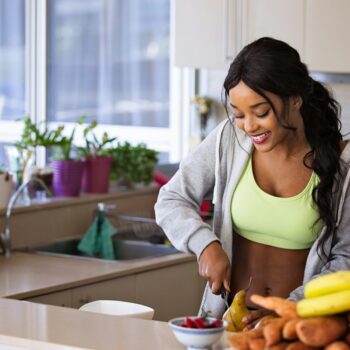 Smiling woman preparing fresh fruit in a sunlit kitchen, embodying a healthy lifestyle.