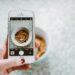 A hand holding a smartphone taking a photo of a bowl of cereal.