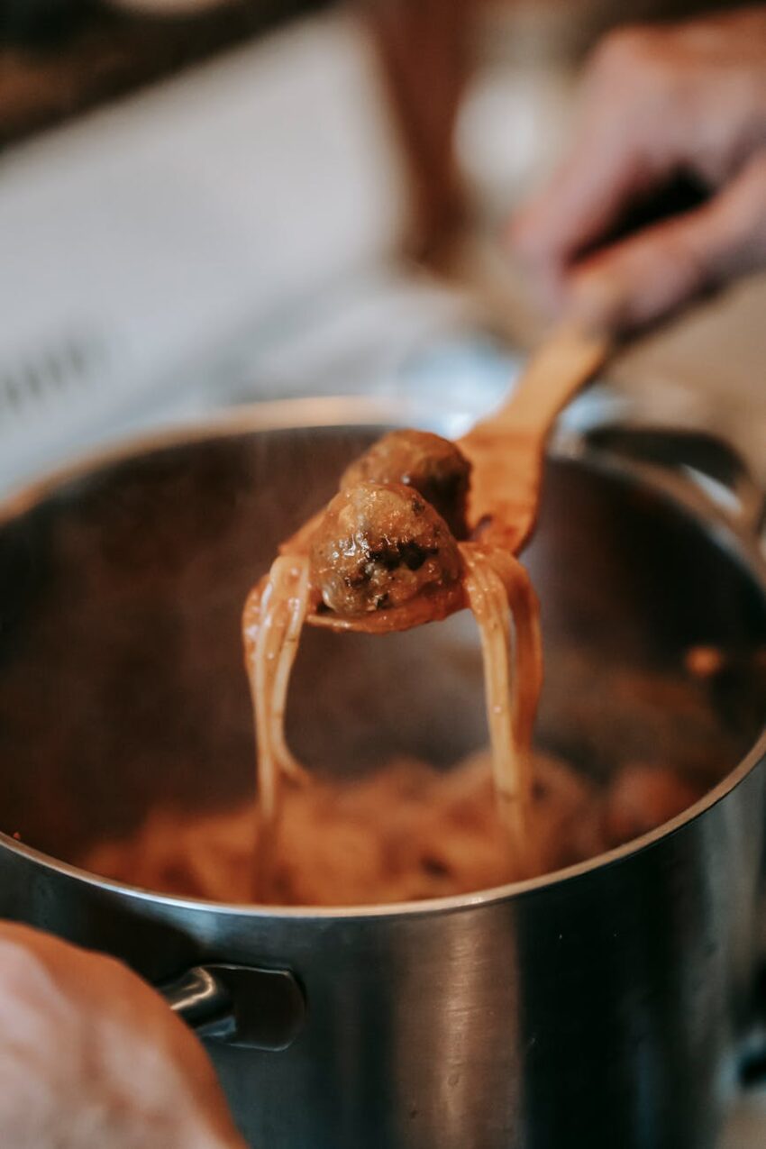 crop person preparing delicious spaghetti with meatballs in kitchen