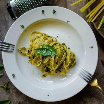 A tempting plate of basil pesto pasta garnished with cheese, surrounded by fresh ingredients.