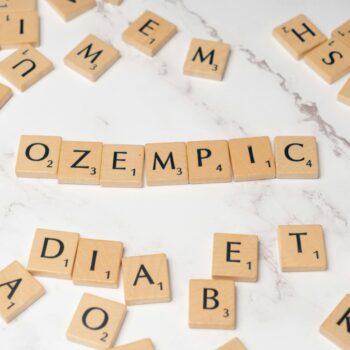 Scrabble tiles spelling Ozempic and diabetes on a marble surface.