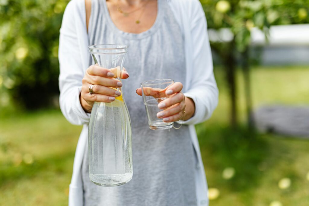 A woman holding a pitcher of water and a glass in a sunny outdoor setting.