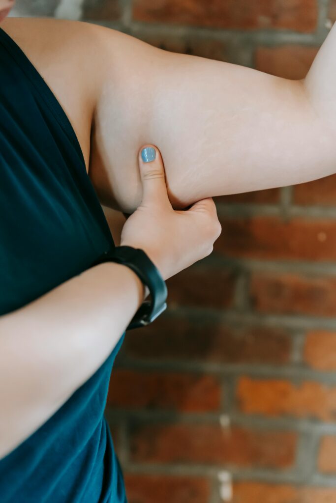 A woman pinches her tricep skin to evaluate body fat in a fitness context.