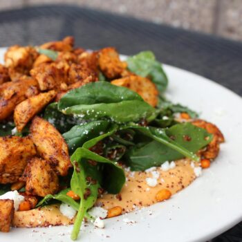 Delicious chicken salad with spinach, feta cheese, and creamy sauce on a white plate.