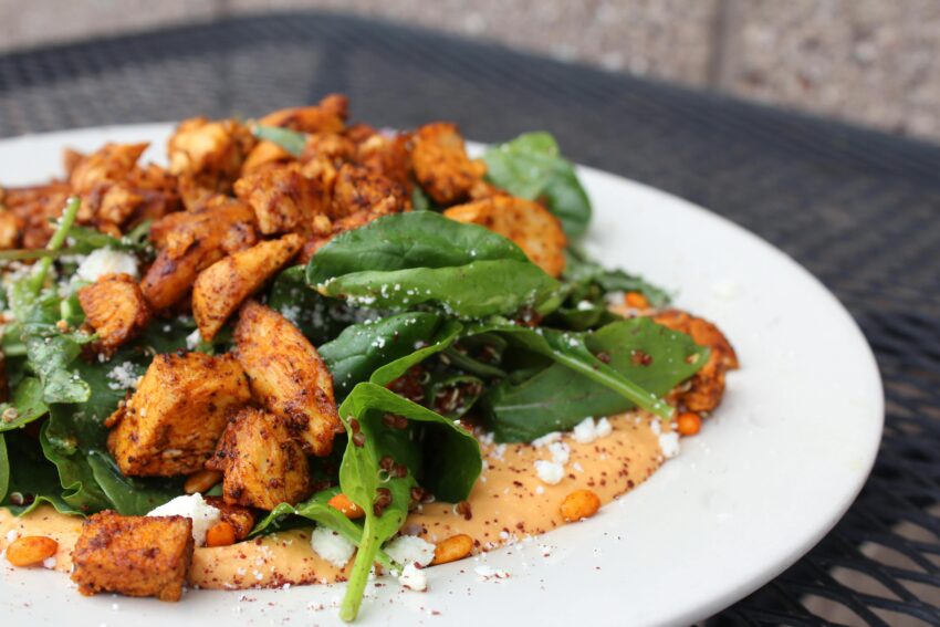 Delicious chicken salad with spinach, feta cheese, and creamy sauce on a white plate.